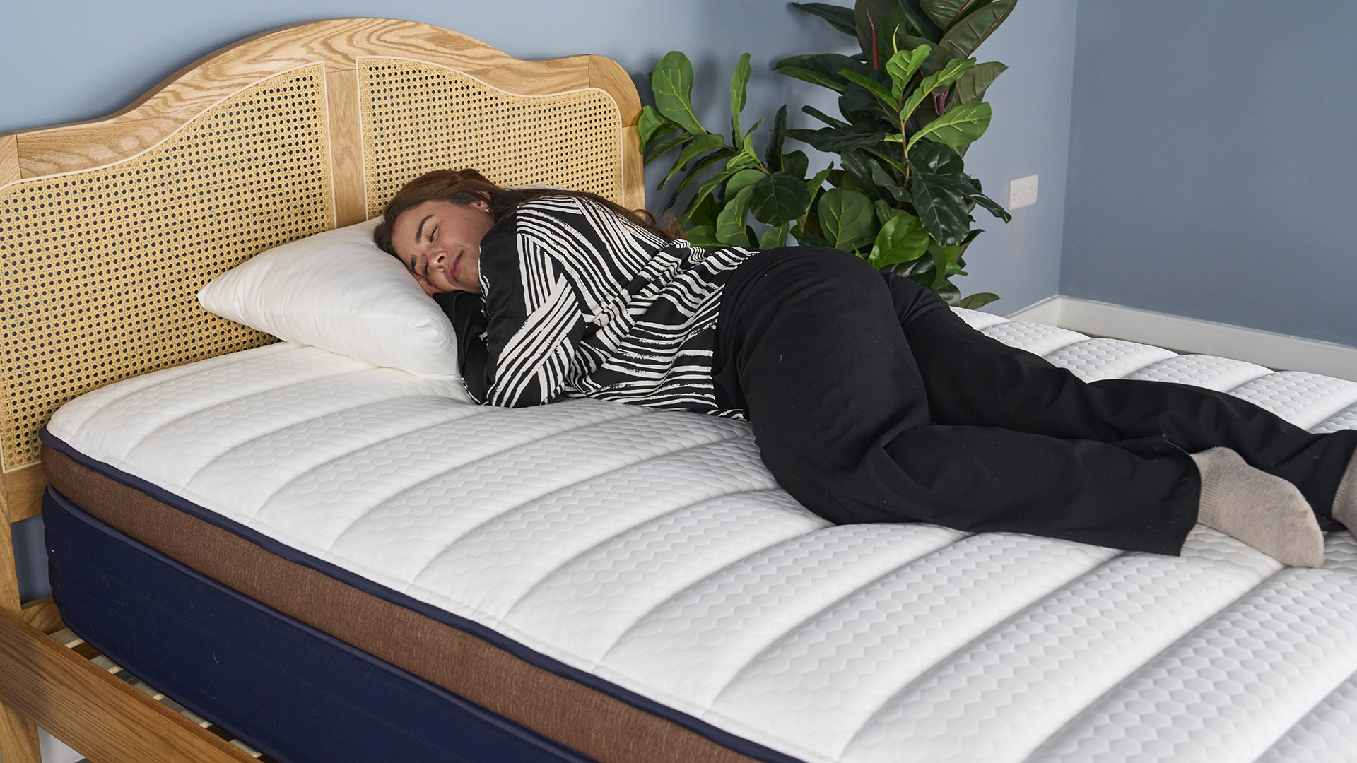 A girl wearing black and white pyjamas laying on her side on Brooklyn Bedding CopperFlex Pro Hybrid mattress with white surface and rattan bedframe
