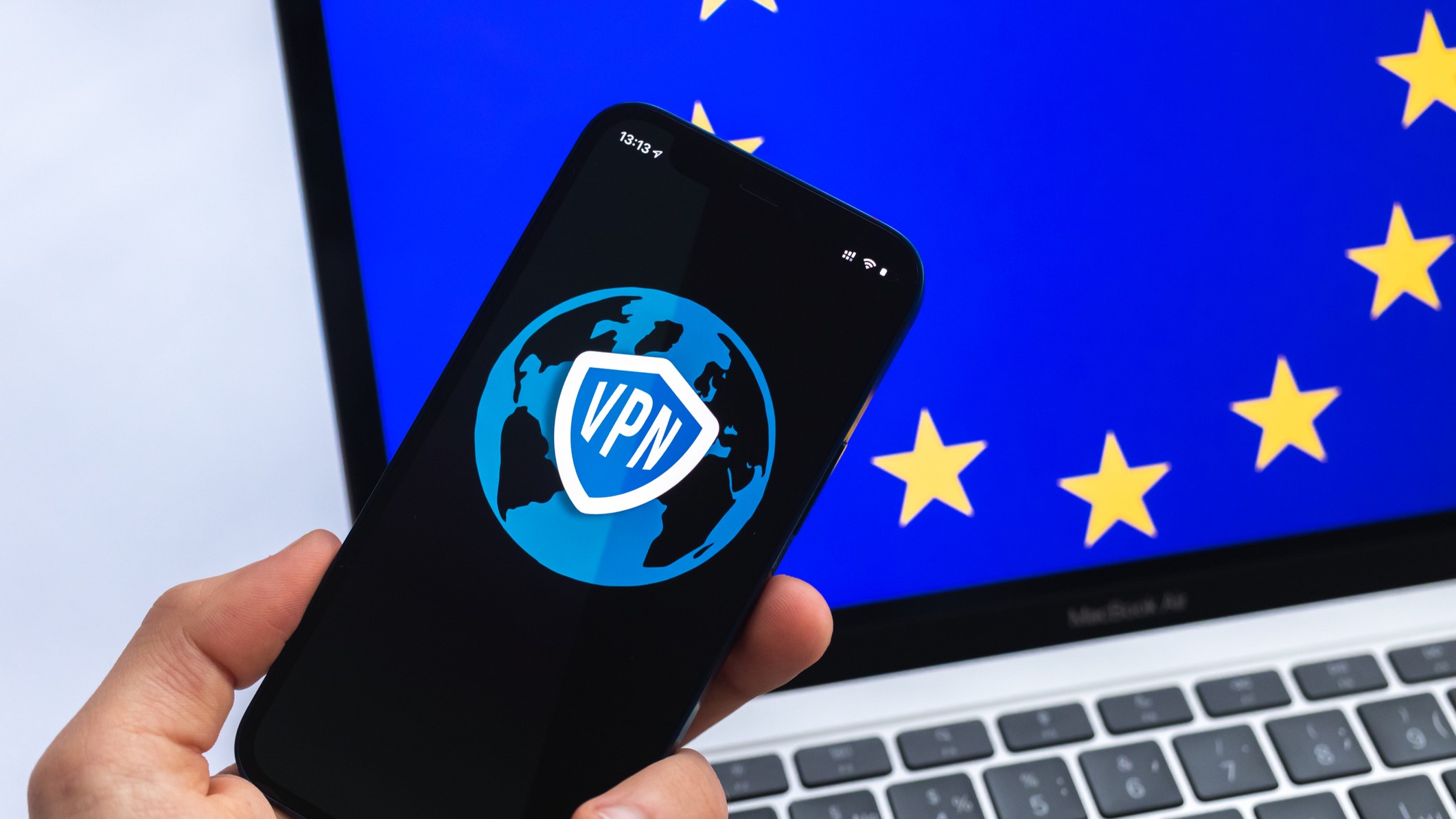 Hand with mobile phone and VPN application with the EU flag on a laptop&#039;s screen on the background