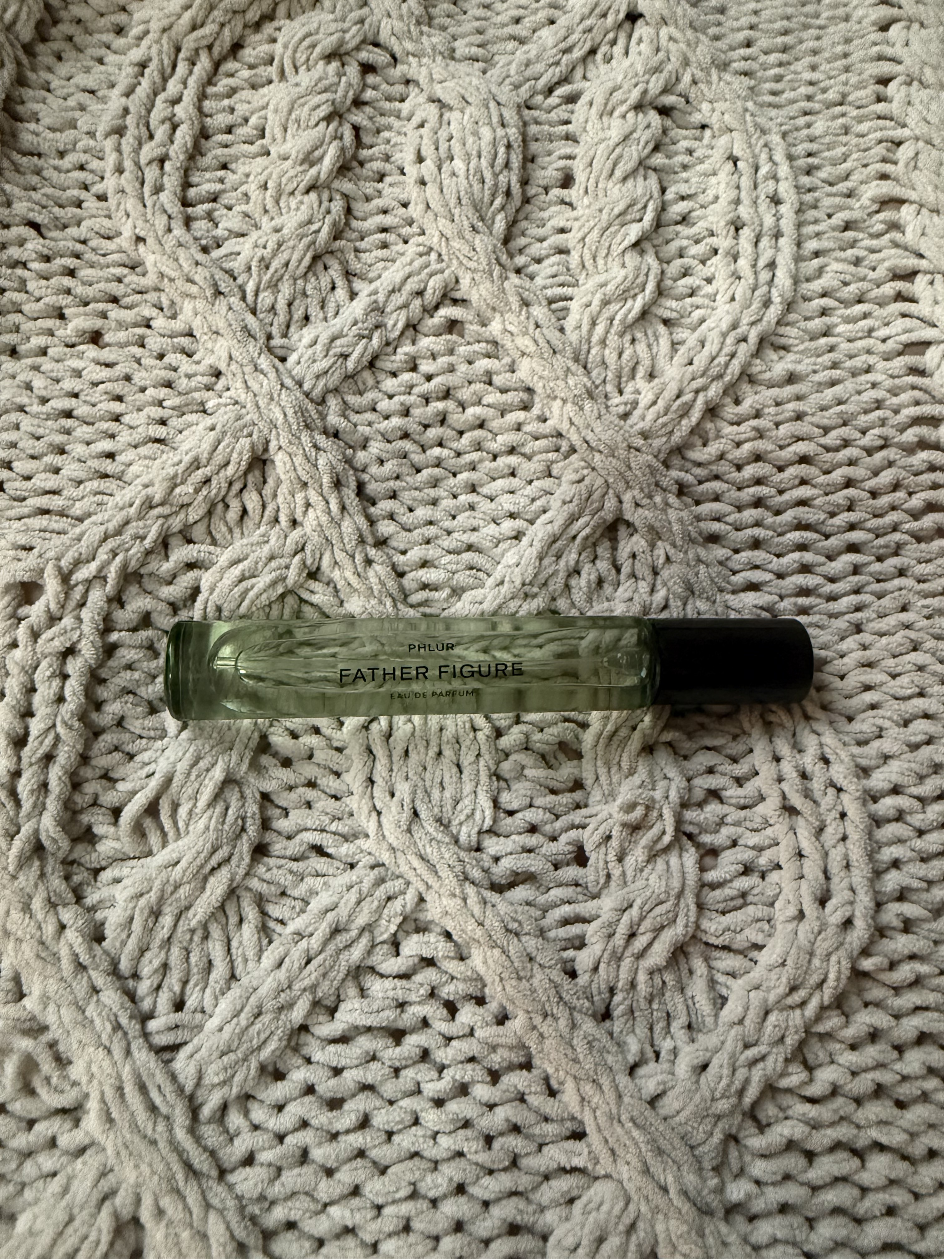 Phlur father figure travel bottle on a grey weave blanket