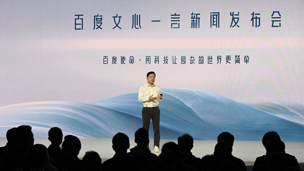 Baidu CEO Robin Li, standing on stage in front of large Chinese text at the Ernie Bot AI press event