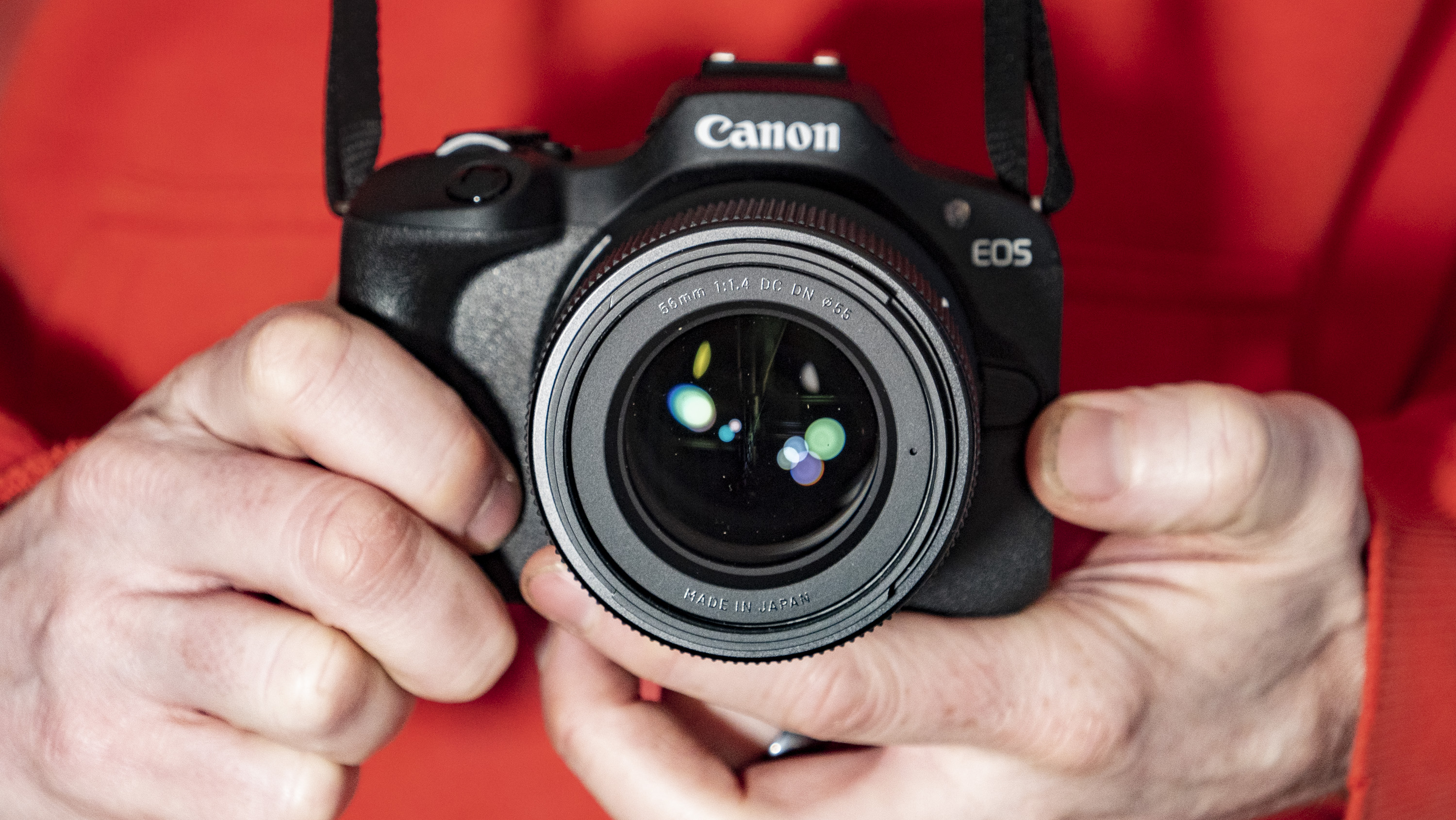 Sigma 56mm F1.4 DC DN Contemporary lens in the hand attached to a Canon EOS R100