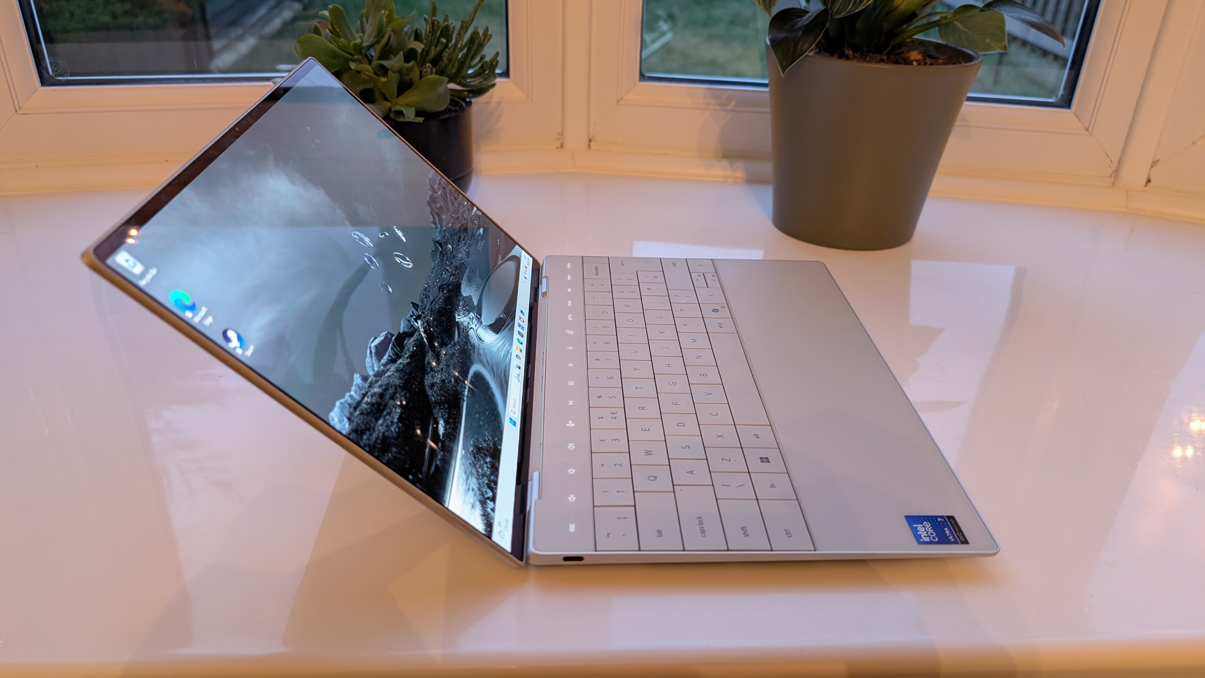 The Dell XPS 13 pictured on a white surface in front of a window with two potted plants.