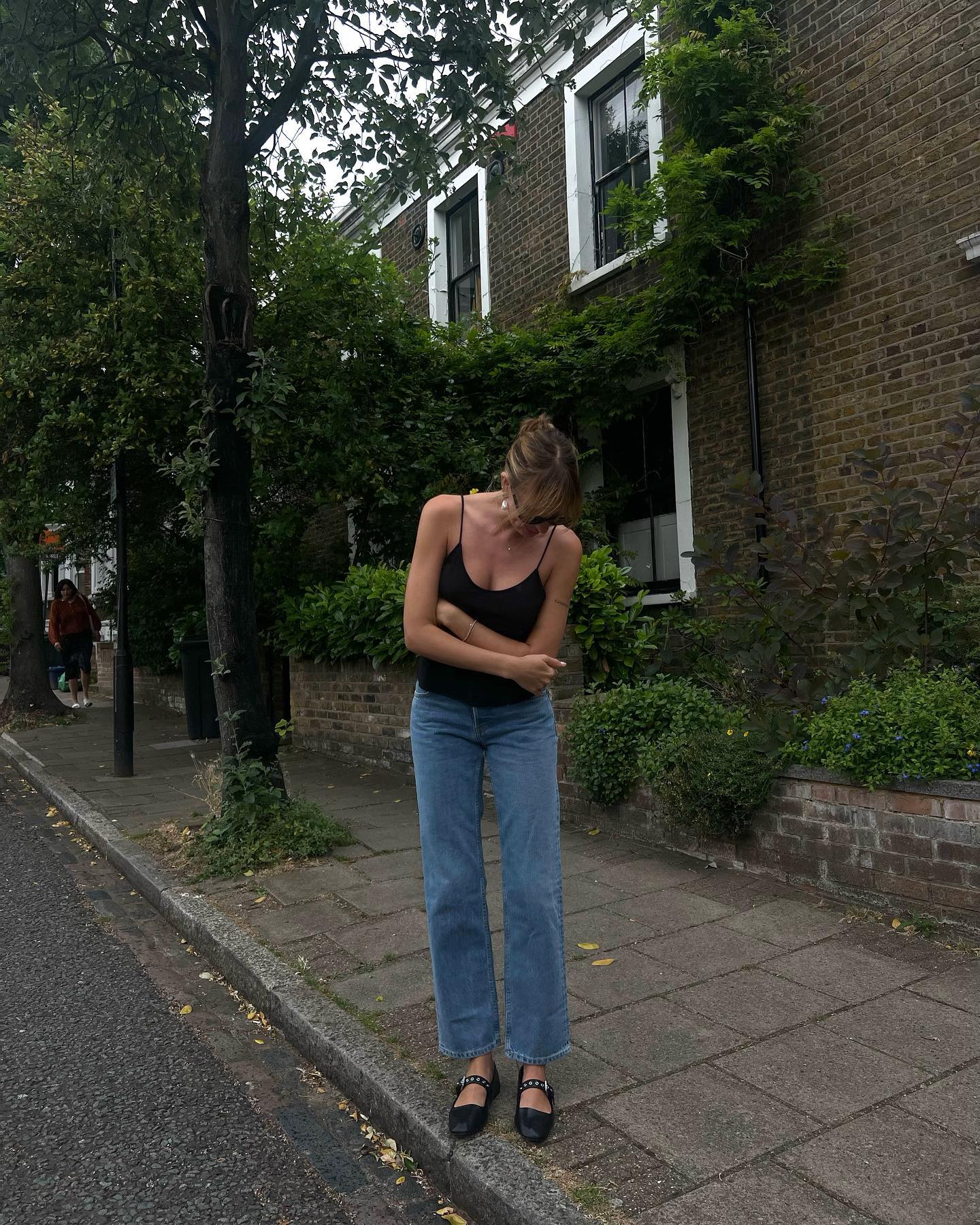 Woman wearing a black tank top, blue jeans, and black ballet flats.
