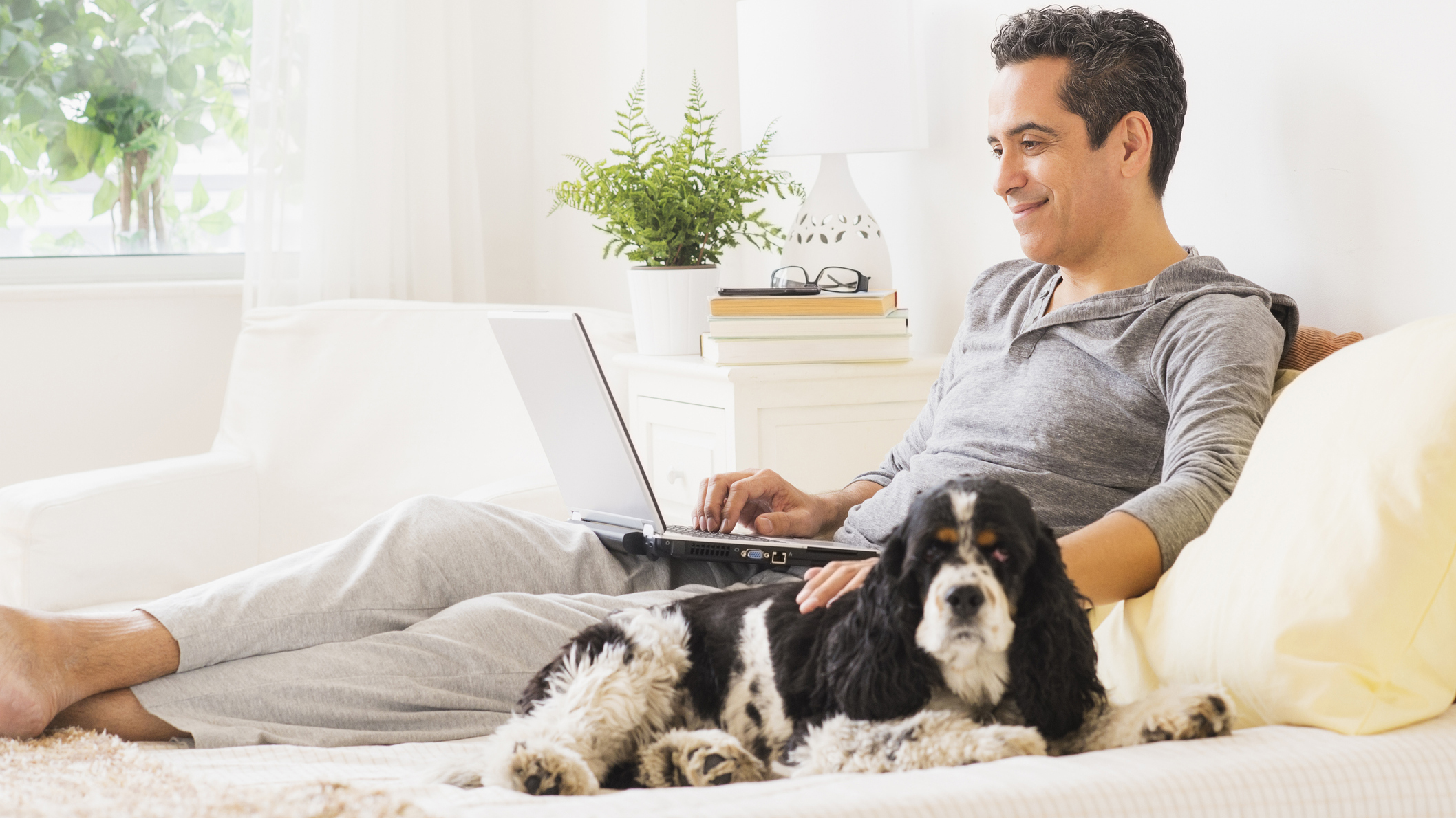 A man lies on his bed with his dog while shopping for a new mattress