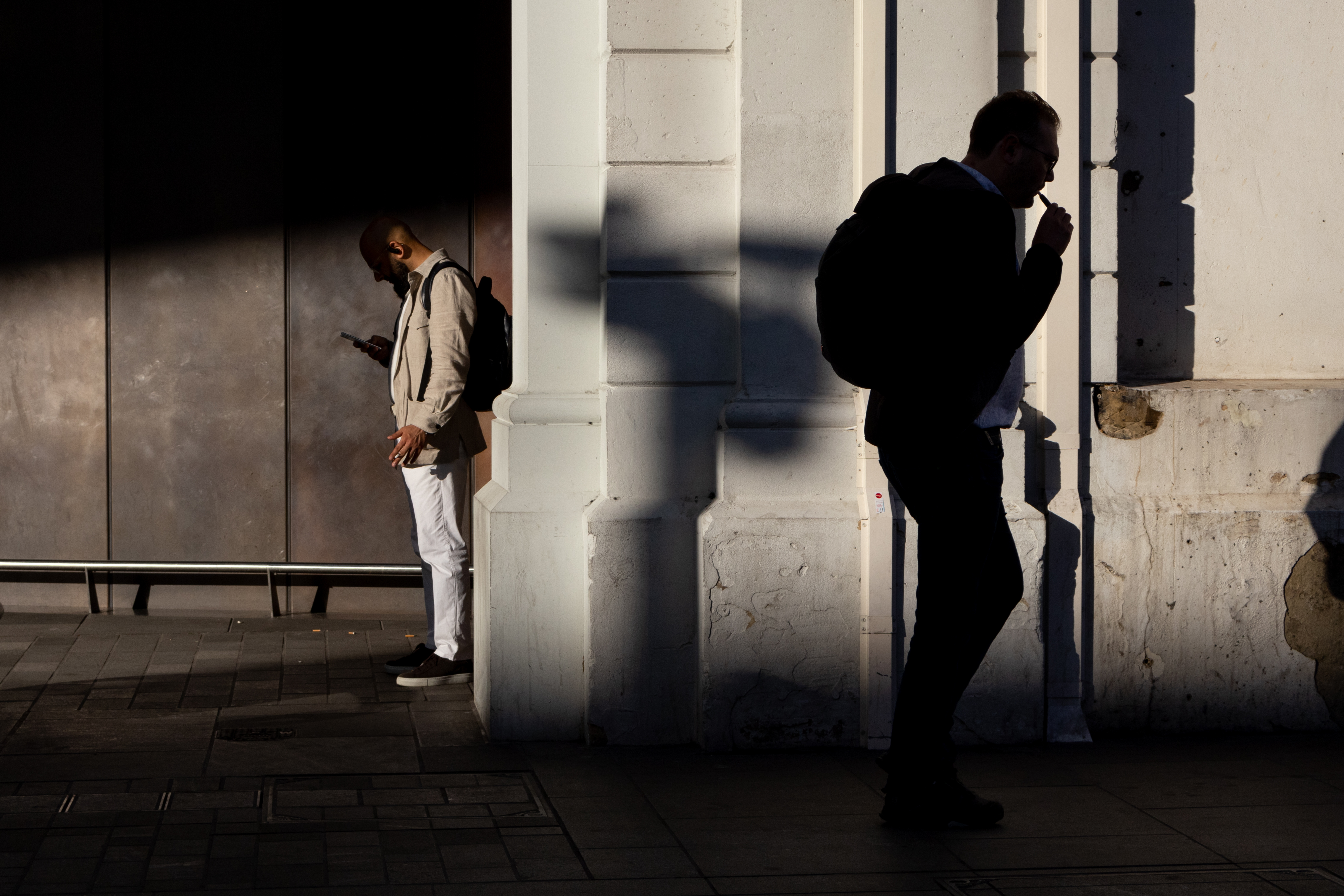 A man standing in the shade at a station reading his phone
