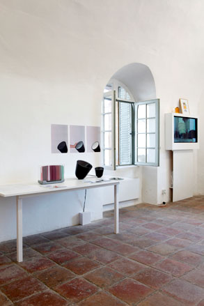 Objects displayed on a white table attached to a white wall with wall art and next to an open french window