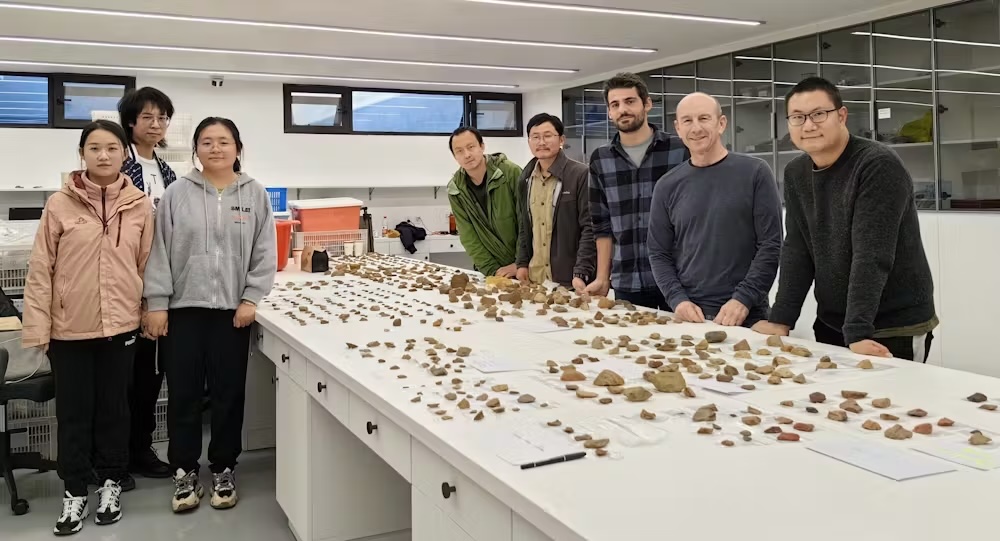 A group of people stand around a table filled with stone tools