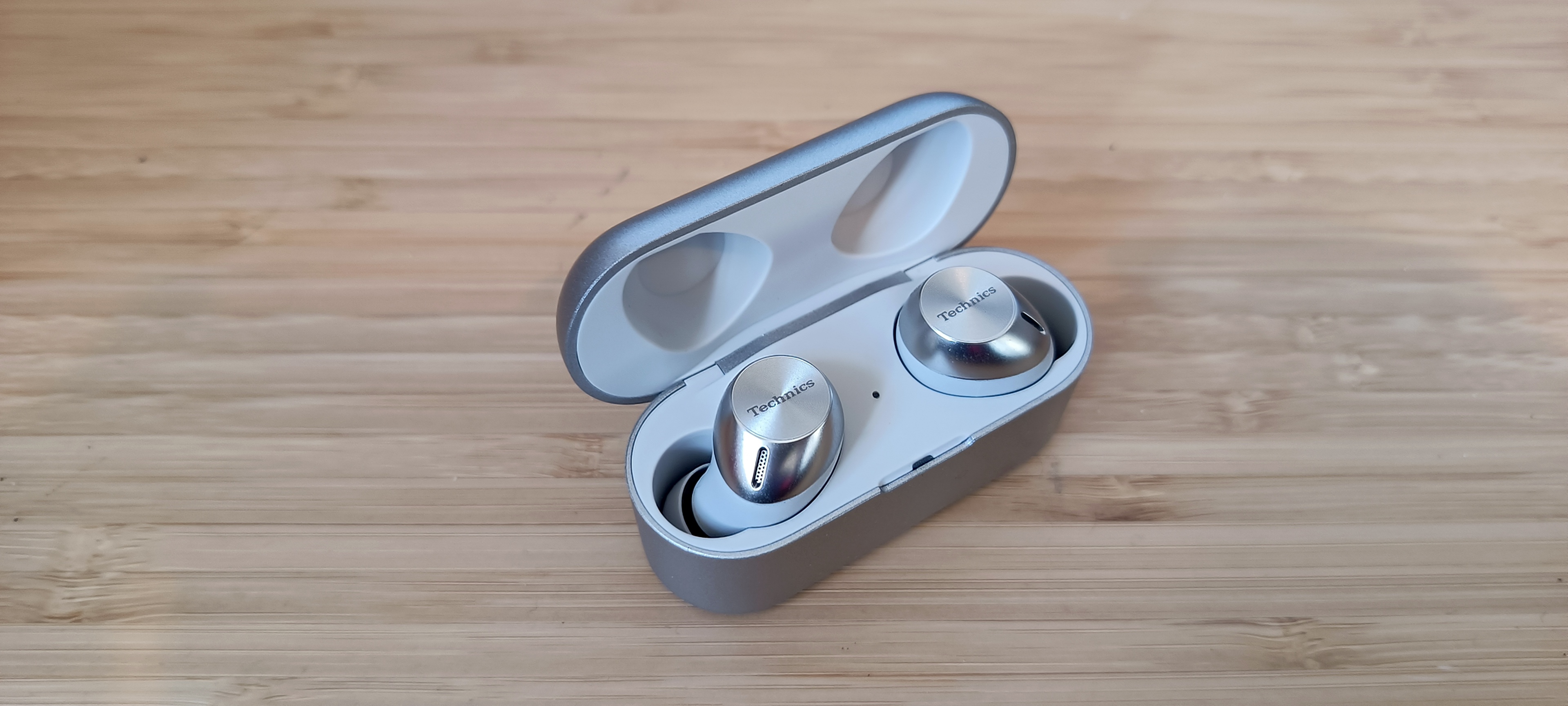 A pair of silver Technics EAH-AZ40M2 earphones on a wooden table