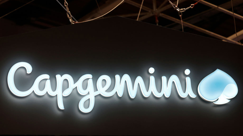 The Capgemini logo (cursive letters that read Capgemini next to a stylised shape that resembles a clover or water drop) lit up in blue against a dark wall.