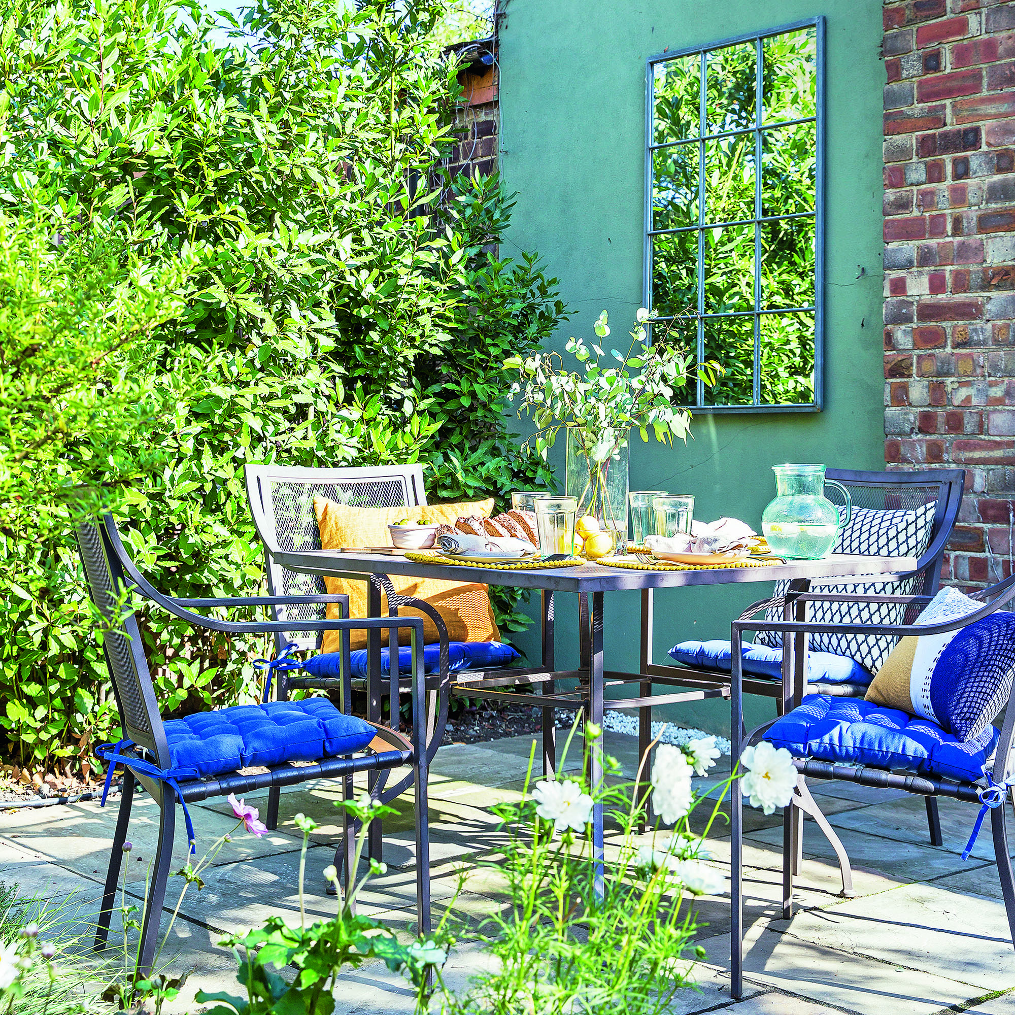 Garden with table and chairs set and garden mirror on brick wall.