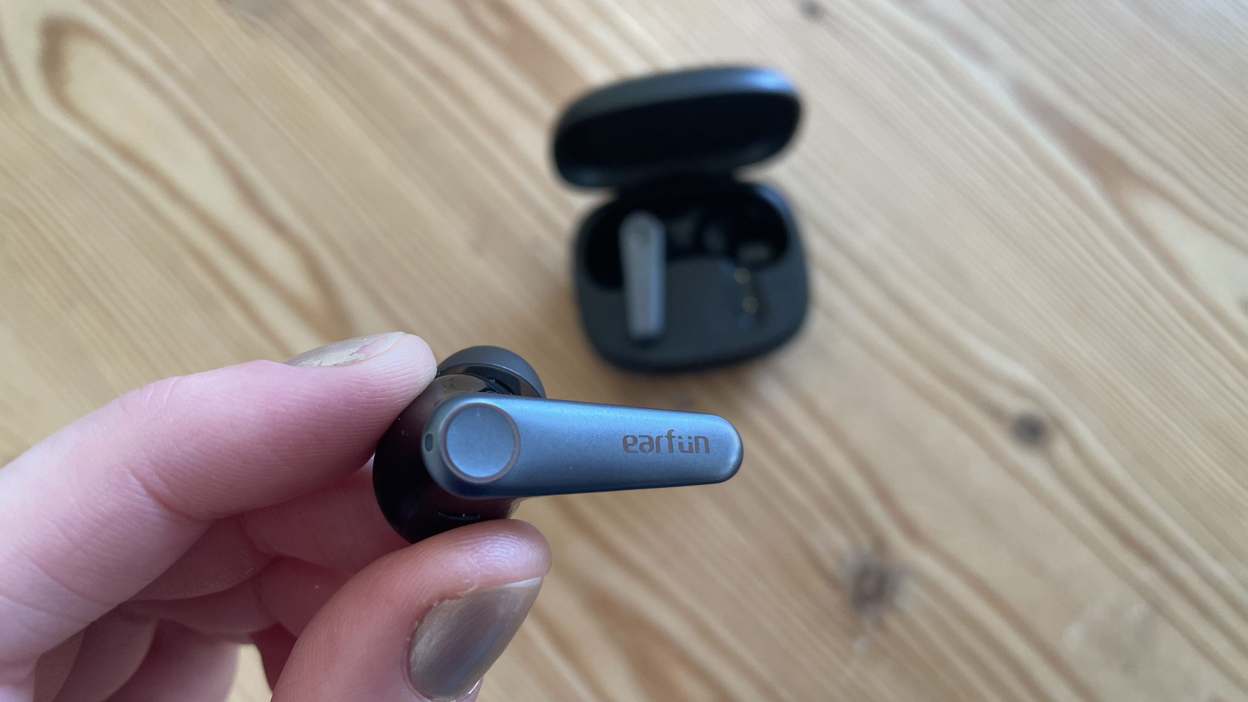 Earfun Air Pro 3 buds held in a hand above a wooden table