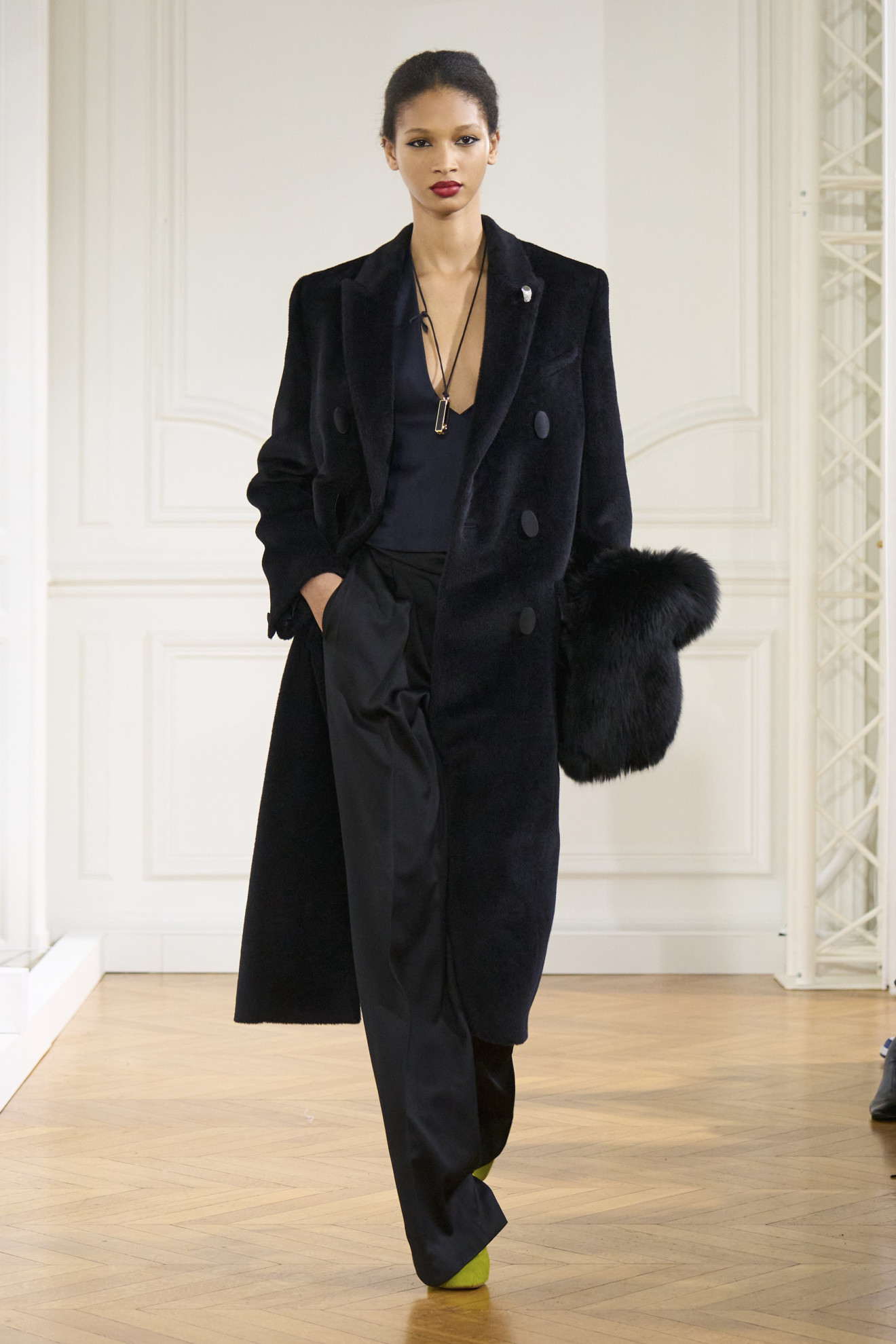 Givenchy model wearing black coat, black pants, low cut top, and long necklace