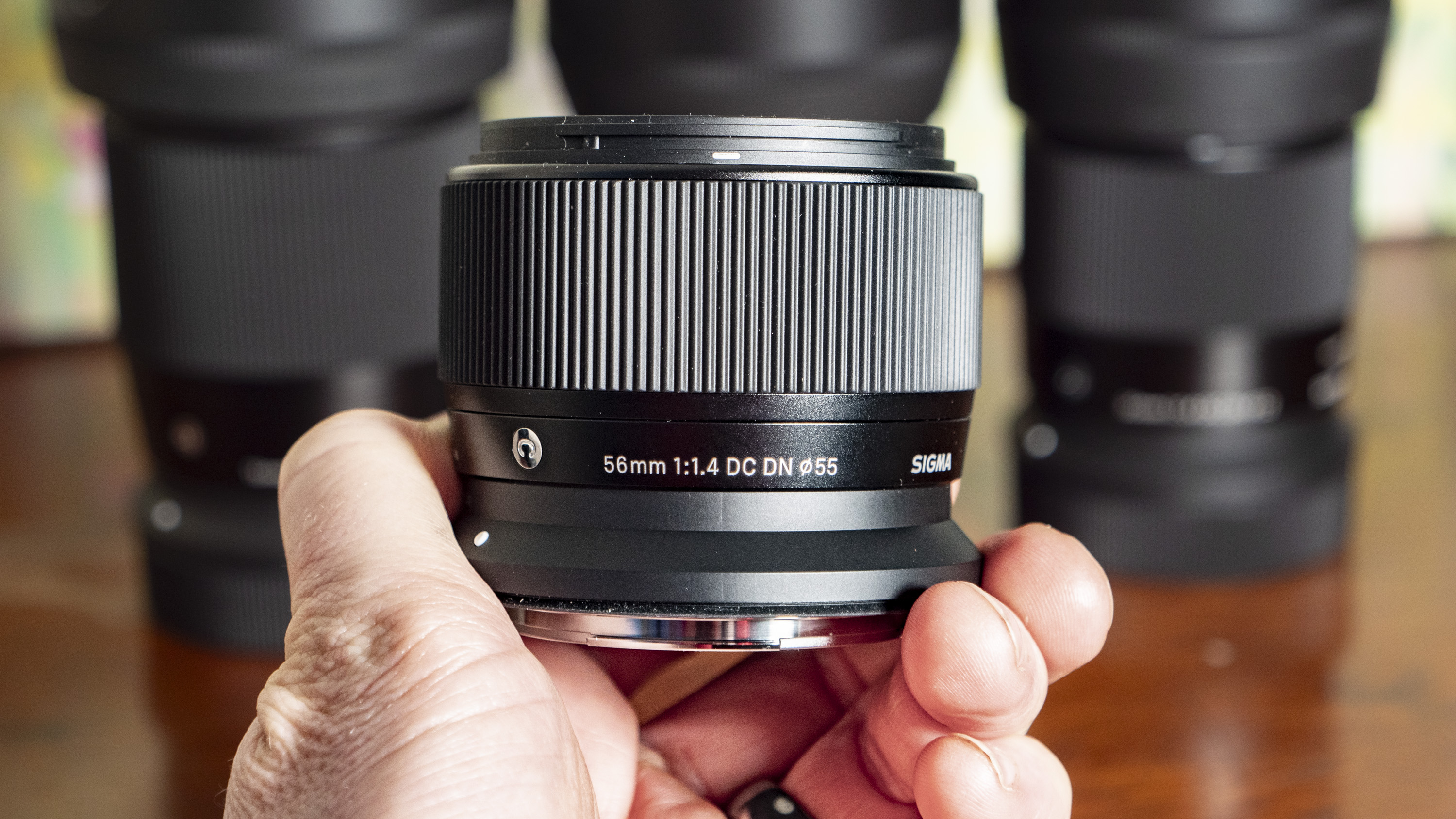 Sigma 56mm F1.4 DC DN Contemporary lens in the hand with other Sigma lenses in the background