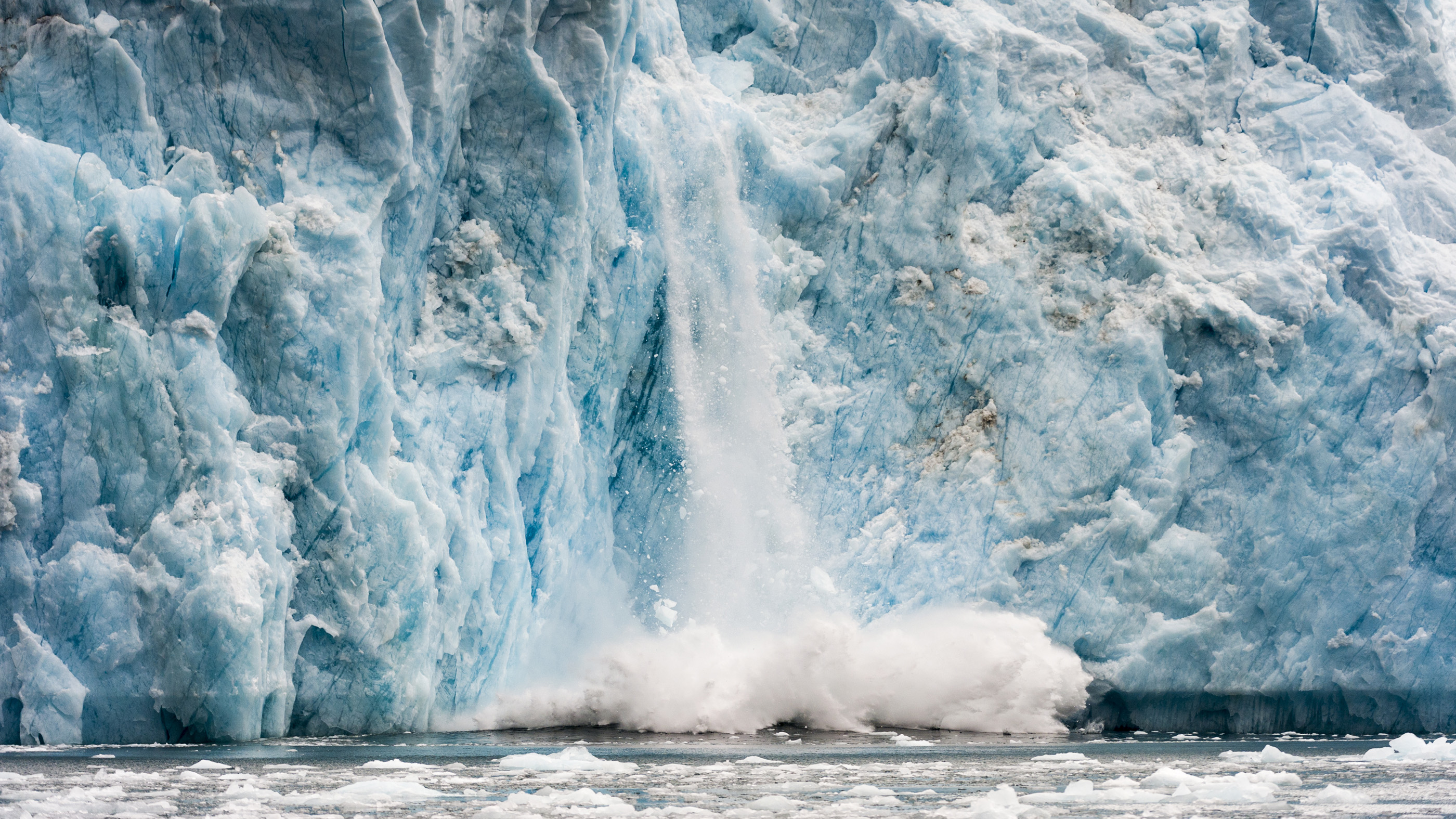 Ice calving from the fracture zone of a glacier crashes into the ocean in Greenland. Melting of such glacial ice is leading to the warping of Earth&#039;s crust.