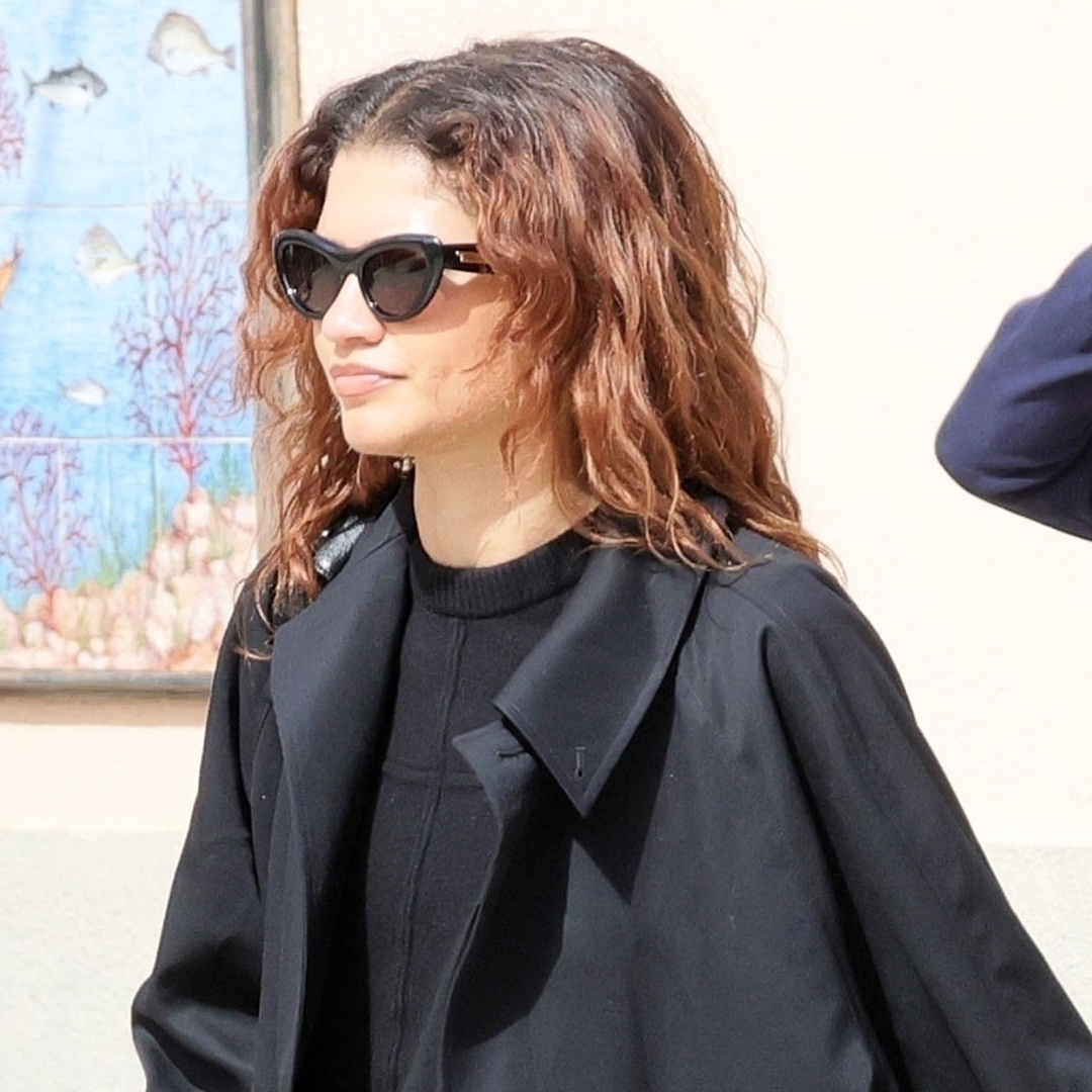 Zendaya walks in Italy wearing a black trench coat with straight leg jeans and boots