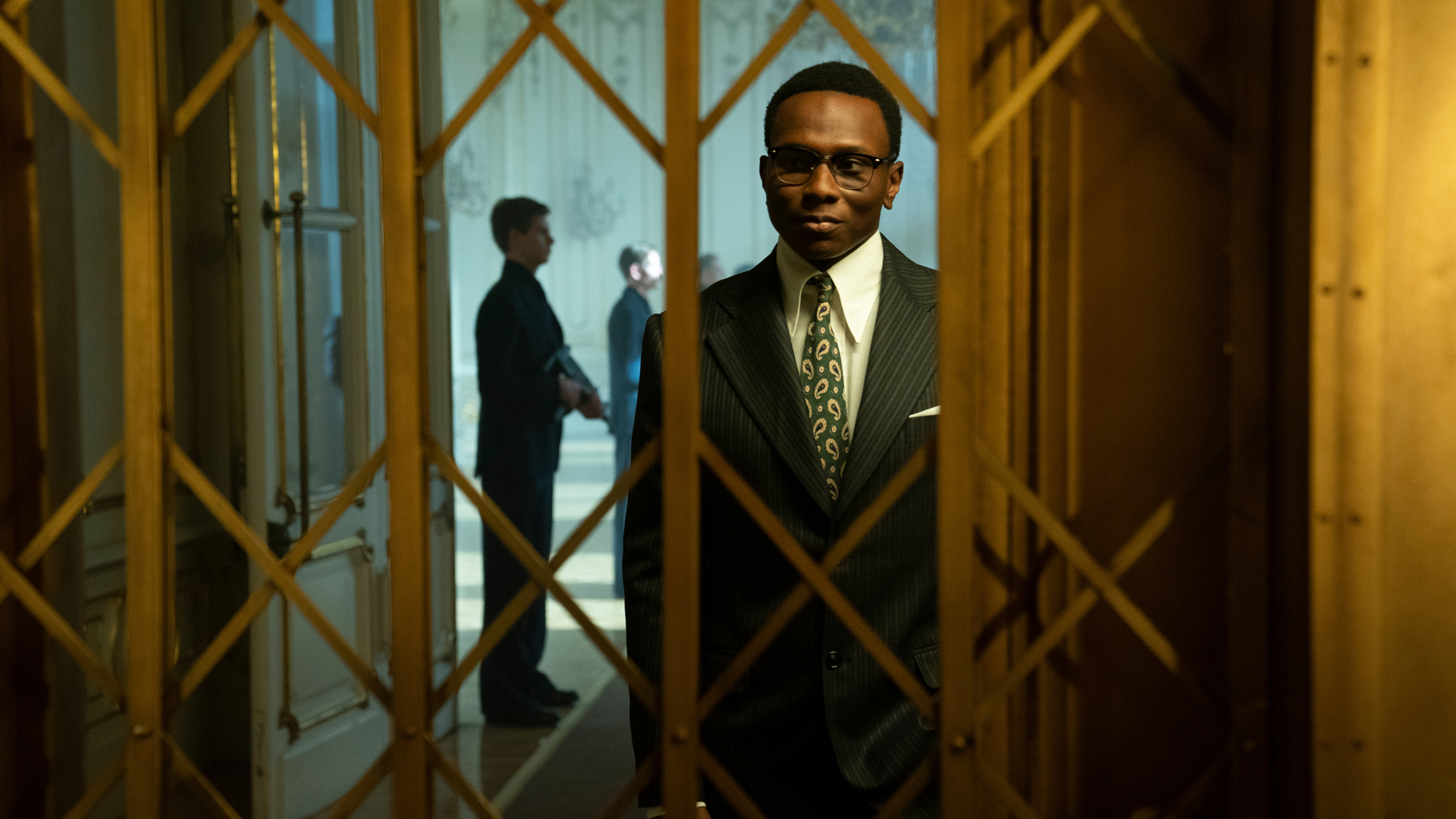 Charon smiles at someone as they ride an elevator in The Continental TV show