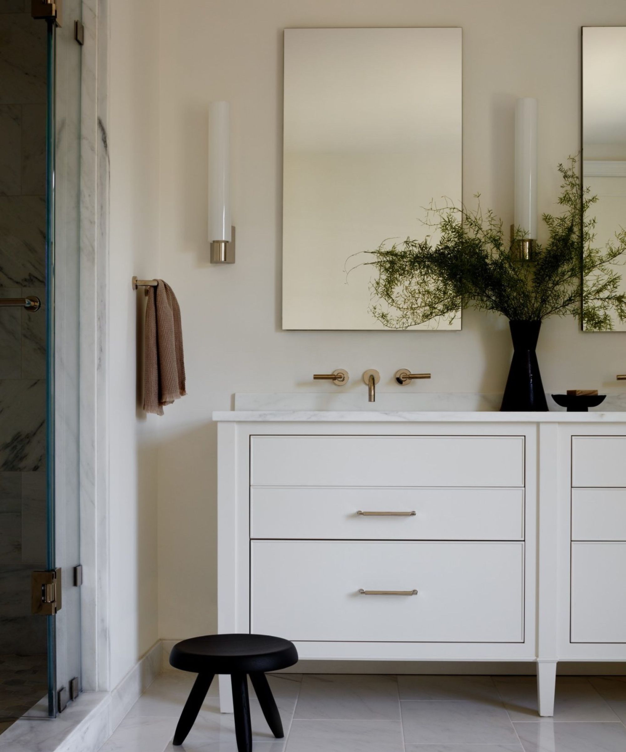 A minimalist bathroom with a white vanity, black stool, simple rectangular wall mirrors, and modern lighting